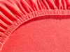 A close-up view of a coral-colored fitted sheet, showing the elasticized edge. Produktbild-Vorschau