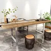 A modern dining or work table with a live edge wooden top and metal legs, set in a stylish room with decorative items and stools.