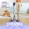 A woman is vacuuming with a cordless stick vacuum cleaner, while a golden retriever lies on the floor nearby. Voir les images du produit