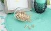 A glass jar filled with mini wooden clothespins is tipped over on a turquoise placemat, with a framed picture and a teal candle holder in the background. Náhled obrázku produktu