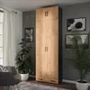 A tall, wooden wardrobe with black accents stands in a room with plants and artwork on the wall. Anteprima dell’immagine prodotto
