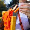 A person is loading a dart into a Minecraft-themed NERF blaster. Podgląd zdjęcia produktu