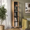 A tall, narrow bookshelf filled with books and decorative items, placed in a living room setting next to a window and a sofa. Anteprima dell’immagine prodotto