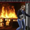 A woman is exiting a burning house, carrying a fire-resistant document bag. The house is engulfed in flames. Voir les images du produit