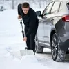 A man is shoveling snow next to a car. Produktbild-Vorschau
