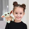 A young girl with her hair in buns is smiling, with a Grogu plush toy sitting on her shoulder. Voir les images du produit