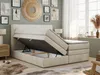 A bedroom scene featuring a beige boxspring bed with its storage compartment open, revealing the mattress mechanism. The room is decorated with artwork and has a window with curtains. Produktbild-Vorschau