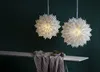 Two white paper star lanterns hang against a dark green wall, with a table covered in a linen cloth in the foreground. Podgląd zdjęcia produktu