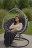 A woman is relaxing in a hanging egg chair outdoors, covered with a blanket. Anteprima dell’immagine prodotto