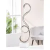 A silver spiral sculpture on a white marble base is displayed on a white surface, with a blurred background of a window and a chair. Produktbild-Vorschau