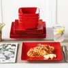 A stack of red square plates and bowls, a plate of spaghetti, and a glass of water with lemon. Náhled obrázku produktu