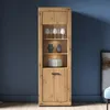 A wooden display cabinet with glass shelves and a drawer, set against a blue wall. Produktbild-Vorschau