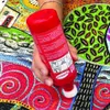 A hand is holding a red bottle of puzzle glue over a colorful puzzle. Náhľad obrázku produktu