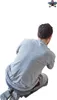 A person is crouching down, viewed from behind, with a white background. A small object is visible in the upper right corner. Voir les images du produit
