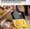 A hand is using a spatula to scrape melted cheese from a raclette pan onto a plate with potatoes and pickles. Produktbild-Vorschau