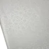 A close-up, angled view of a white tablecloth with a subtle floral damask pattern. Produktbild-Vorschau
