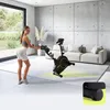 A woman is posing next to a stationary bike in a modern living room. Produktbild-Vorschau
