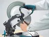 A person's hands are shown operating a miter saw. Podgląd zdjęcia produktu