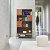 A woman walks down a hallway past a bookshelf filled with decorative items. Produktbild-Vorschau
