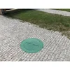 A green manhole cover is placed on a cobblestone path next to a patch of grass. Produktbild-Vorschau