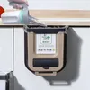 A hand is using a scoop to put waste into a hanging trash can in a kitchen. Náhľad obrázku produktu