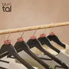 A row of black wooden hangers with cedar wood moth repellent rings, hanging on a wooden rod against a textured light brown wall. Anteprima dell’immagine prodotto
