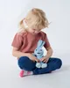 A young girl sits cross-legged on a white floor, holding a blue plush bunny. Náhľad obrázku produktu