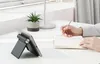 A person is writing in a notebook next to a tablet stand on a desk. Náhľad obrázku produktu