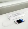 A white power strip with multiple outlets and USB ports is shown on a white surface, with a smartphone connected to it via a white cable. Náhled obrázku produktu
