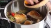 A person is adding ingredients to a large pot of food on a stove. Produktbild-Vorschau
