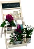 A wooden, multi-tiered plant stand with various potted plants and decorative items, including a watering can and jars. Produktbild-Vorschau