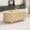 A light wood coffee table with ribbed doors and copper handles sits on a textured rug in a living room setting. A small plant and a book are on top of the table. Voir les images du produit