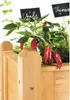 A close-up of a wooden herb planter with chili peppers and herbs growing in it. Small chalkboards with plant names are visible. Produktbild-Vorschau