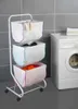 A laundry sorter with three baskets next to a washing machine. Produktbild-Vorschau