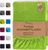 A folded green fitted sheet is displayed with a swatch of other colors to the left. A brown paper band wraps around the middle of the sheet with product information printed on it. Produktbild-Vorschau