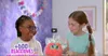 Two young girls are interacting with a small, fluffy toy creature. The background is decorated with colorful pom-poms and has a dreamy, ethereal quality. Náhľad obrázku produktu