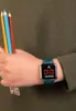 A person's wrist wearing a digital watch and holding colored pencils. Produktbild-Vorschau
