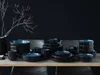 A dark and moody table setting with a large dinnerware set and a decorative branch. Produktbild-Vorschau