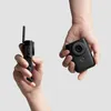 Two hands holding a compact camera and a selfie stick against a light gray background. Podgląd zdjęcia produktu