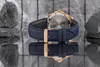 A close-up shot of the back of a watch with a blue leather strap and gold buckle, resting on a reflective surface with rocks in the background. Voir les images du produit