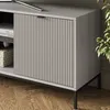 Close-up of a modern gray TV stand with a fluted door and black metal legs, placed on a wooden floor. Náhled obrázku produktu