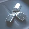 A pair of car keys with a fob attached, resting on a dark, textured surface, likely leather. Anteprima dell’immagine prodotto