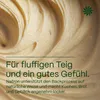 Close-up of a creamy, swirling substance, likely dough or batter, with green text overlay and a green floral logo. Produktbild-Vorschau