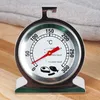 A close-up of a stainless steel oven thermometer with a dial and red pointer, placed on a wooden surface with a textured gray fabric in the background. Produktbild-Vorschau