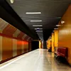 A modern subway station platform with orange and white striped walls, a polished concrete floor, and red benches. Produktbild-Vorschau