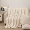 A cream-colored sherpa blanket is draped over a sofa, with two matching pillows placed in the foreground. Podgląd zdjęcia produktu