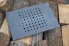 A rectangular cast iron grate with many holes is placed on a pile of chopped wood. Náhled obrázku produktu