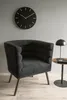 A dark gray armchair sits next to a small side table with a lamp on it, in front of a gray wall with a black clock. Náhled obrázku produktu