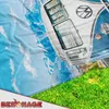 A close-up view of a Volkswagen T1 bus on a blanket with a mountain and sky print, and a grassy foreground. Produktbild-Vorschau