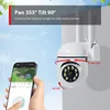 A hand holding a smartphone displaying a live feed from a security camera, with the camera itself mounted on a wall. Produktbild-Vorschau